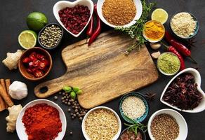 Various spices in a bowls and empty cutting board on black concrete background. Top view copy space. photo