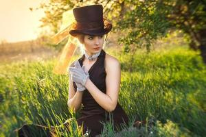 young blonde girl in a brown vintage dress and top hat reads a book photo