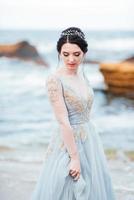 bride in a blue light dress walking along the ocean photo