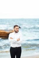 groom in a white shirt and black pants by the ocean photo