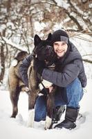 A man in a jacket and a knitted hat walks with an American Akita dog photo