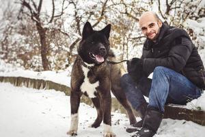 A man in a jacket and a knitted hat walks with an American Akita dog photo