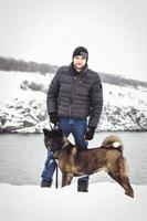 A man in a jacket and a knitted hat walks with an American Akita dog photo