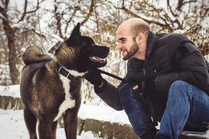 A man in a jacket and a knitted hat walks with an American Akita dog photo