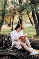 young girl in white clothes sits on a tree in the forest photo