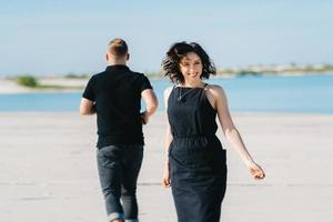 young couple a guy with a girl in black clothes are walking on the white sand photo