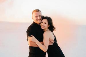 guy and a girl in black clothes hug and run on the white sand photo