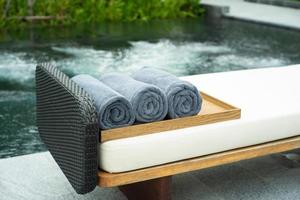 Close up of rolls of towels on the wooden tray on a beach bed with a blurred bubble whirlpool in the background. Spa industry photo