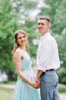 chico feliz con una camisa blanca y una chica con un vestido turquesa están caminando en el parque forestal foto