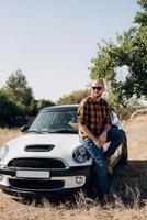 Guy in a plaid shirt next to a white car photo