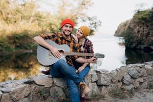 Un chico con un sombrero brillante toca la guitarra con una chica sobre un fondo de rocas de granito foto