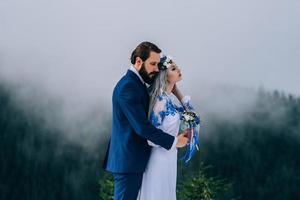 El novio en un traje azul y la novia en blanco en las montañas de los Cárpatos. foto