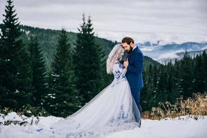 El novio en un traje azul y la novia en blanco en las montañas de los Cárpatos. foto
