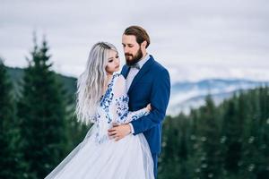 El novio en un traje azul y la novia en blanco en las montañas de los Cárpatos. foto