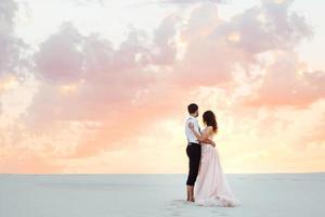 young couple a guy in black breeches and a girl in a pink dress are walking along the white sand photo