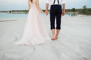 young couple a guy in black breeches and a girl in a pink dress are walking along the white sand photo