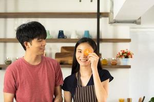 A young Asian couple are eating together and smiling happily while cooking their salad in the kitchen. photo