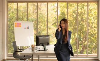 Mujer de negocios asiática mediante teléfono móvil en una oficina.