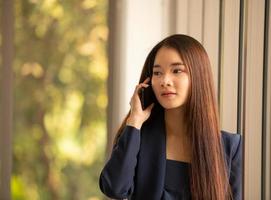 Mujer de negocios asiática mediante teléfono móvil en una oficina.