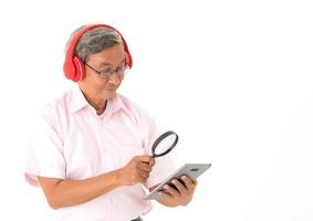 Senior hombre asiático feliz de escuchar música en línea con auriculares y tableta, aislado