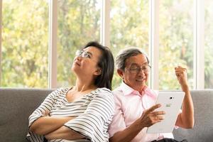 Senior hombre y mujer asiáticos se relajan de vacaciones en el fondo natural de la sala de estar con tecnología moderna foto