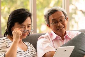 Senior Asian man and woman relax on holiday in the natural living room background with modern technology