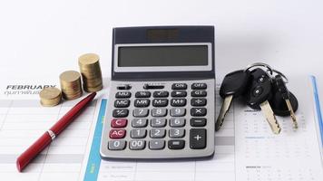 Calculadora y pila de monedas y pluma de negocios y llave de coche en el calendario por concepto de préstamo