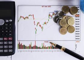 Fountain pen and calculator and coins stack on Stock index chart for finance concept photo