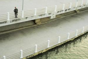 un hombre no identificado se encuentra en la pasarela de hormigón a lo largo de la orilla del río con el reflejo de la luz del atardecer. foto