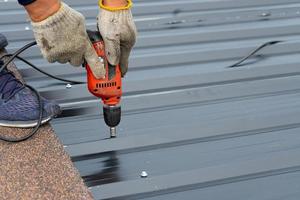 Workers installing a metal sheet roof with an electrical drilling machine. Selective focus on the drilling tool while building the roof photo