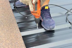 Closeup of hands installing a metal sheet roof with an electrical drilling machine. Selective focus on the drilling tool while building the roof photo