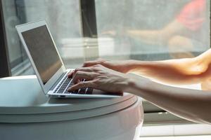 Closeup hands of a man typing on the keyboard of laptop in the toilet with the light of the sun. Work from home concept. photo