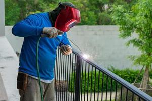 Closeup portrait of welder with mask welding the steelwork of black fence with sparking light and smoke photo