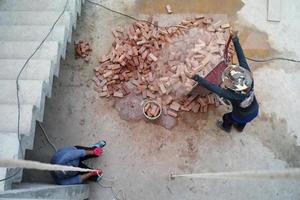 Top view workers working at the construction site. Laborer carries the red brick by the steel cart. photo