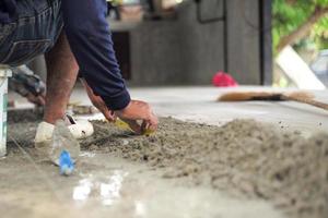 El enfoque selectivo en la pierna y las manos del trabajador midiendo el piso durante la instalación de las baldosas en la casa en construcción foto