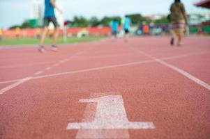 Textura abstracta y fondo de pista de atletismo vacía con el número uno en el suelo y gente desenfocada haciendo ejercicio en segundo plano. foto