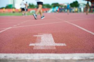 Textura abstracta y fondo de pista de atletismo vacía con el número uno en el suelo y gente desenfocada haciendo ejercicio en segundo plano. foto