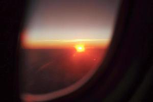 La luz del atardecer en el horizonte con fondo de cielo azul y la sombra de la ventana de un avión en primer plano foto