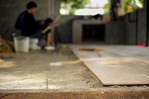 Closeup floor tiles on the mixed cement with nylon for leveling in the house under construction with blurred workers in the background photo