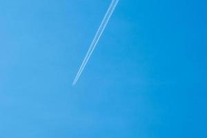 Avión volando en el cielo azul claro con rastro blanco a lo largo de la ruta. foto