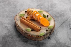 Sliced turmeric with cinnamon, black pepper and cardamom on a wooden slice photo