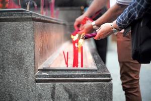 Closeup hands holding the bundle of incenses for lighting with candles in the sand tray photo