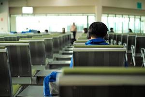 Retrato de espalda del hombre escuchando música con un auricular mientras espera el vuelo en la sala de la terminal de salidas foto