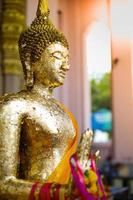 Closeup Buddhist statue coated by the golden leaf and hanging by flower garlands