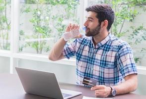 Young businessman is drinking a thirst quencher at home and working on a laptop. Concept of working and doing business online photo