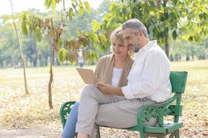 Caucasian elderly couple sits and relaxes on a bench in the park and uses a laptop. Concept of living life happily on the holiday photo