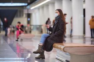 una mujer con una mascarilla médica está esperando un tren y sosteniendo un teléfono inteligente foto