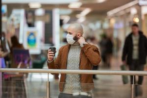 un hombre se pone una máscara mientras sostiene una taza de café en el centro comercial foto