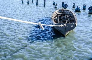 Barco de pesca gris atado con una cuerda en agua azul verdosa