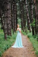 Happy girl in a turquoise long dress in a green park photo